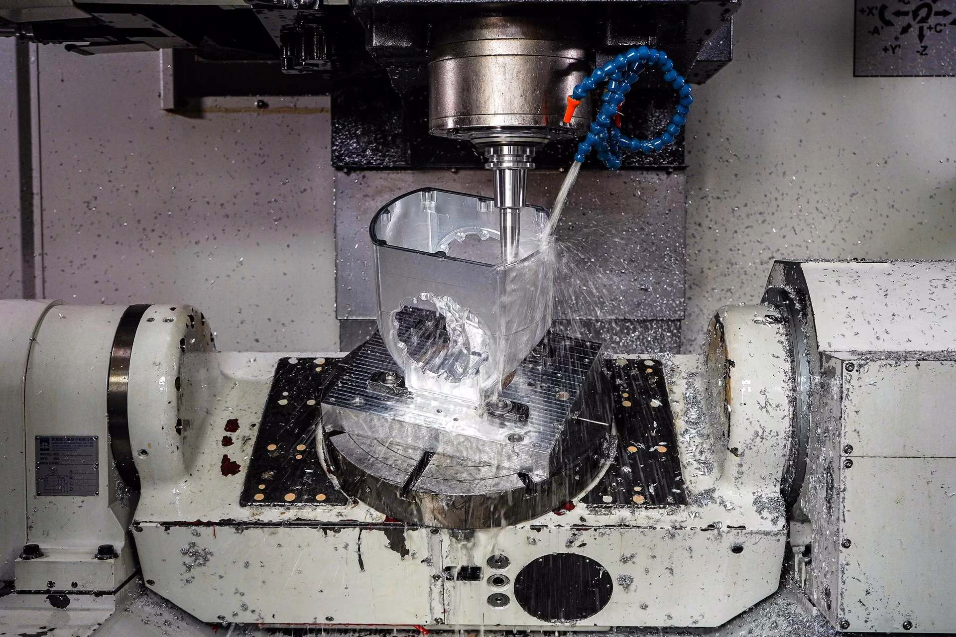 Five-axis CNC machining center cutting an aluminum housing under coolant