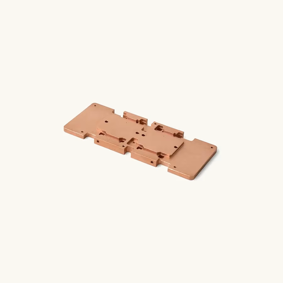 Single machined copper busbar plate with stepped pockets, slots, and mounting holes on a warm neutral background.