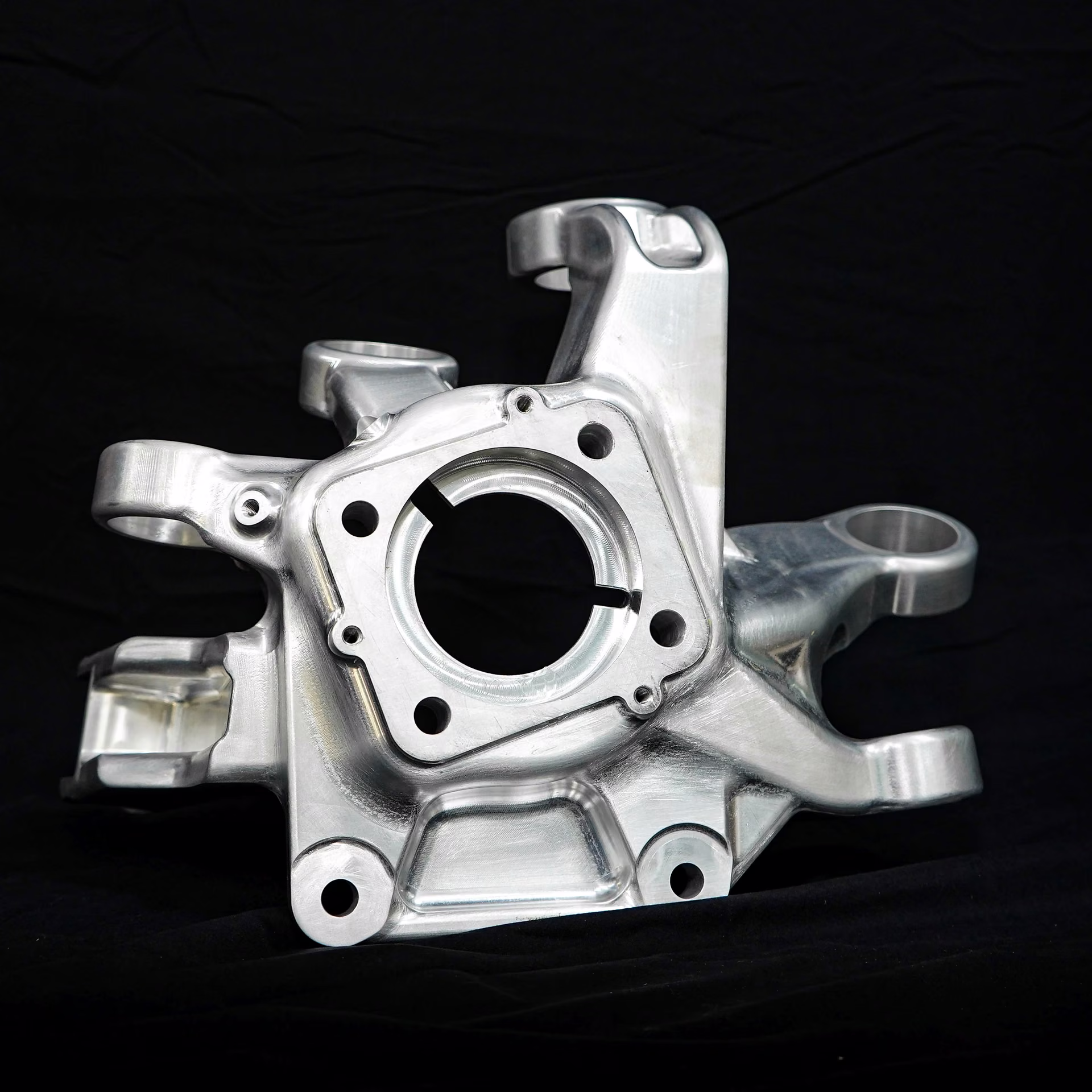 Machined aluminum automotive steering knuckle with a central bearing bore and multiple mounting ears.