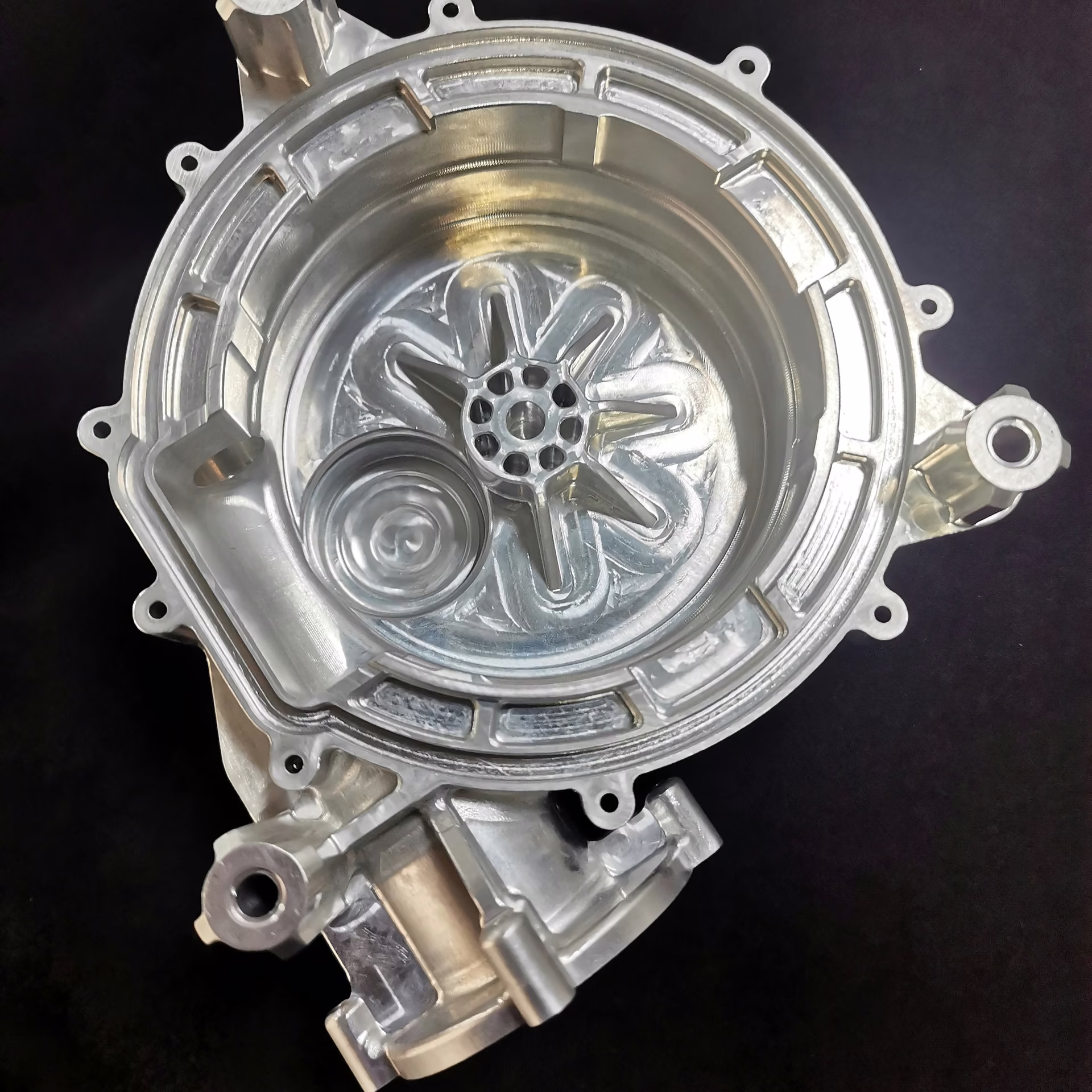 Front view of a machined aluminum turbocharger housing with a circular inlet and internal scroll geometry.