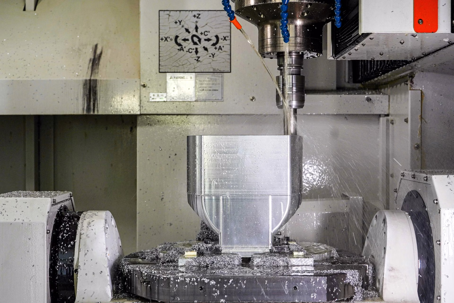 Five-axis machining center cutting a contoured aluminum housing on a rotary fixture