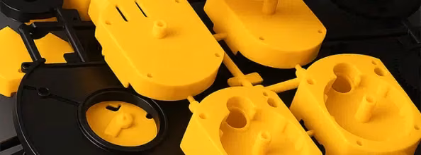 Yellow and black multi-material molded components arranged on a dark workshop surface