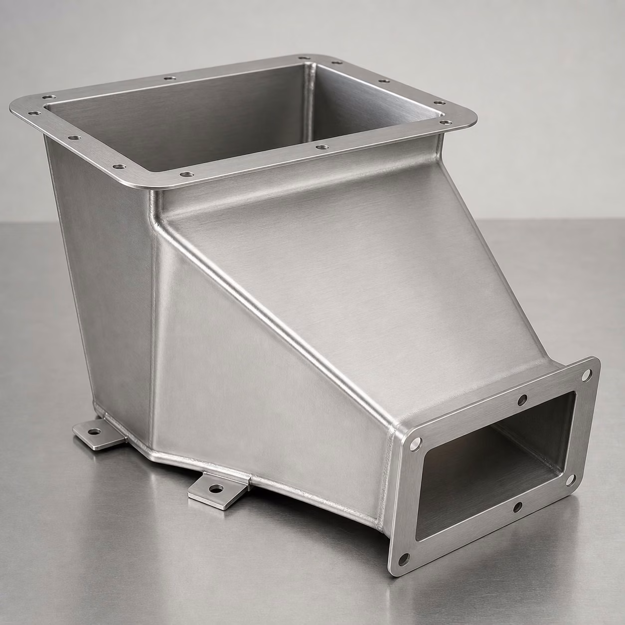 Brushed stainless steel process chute with a rectangular inlet, tapered formed walls, smooth welded seams, outlet flange, and mounting tabs.